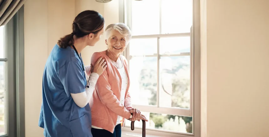 Shot of a young nurse standing with a senior woman next to a window in a nursing home.